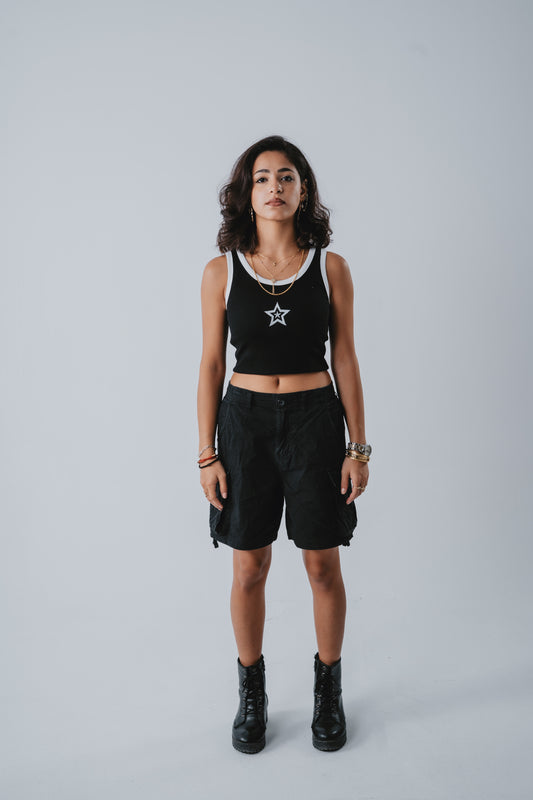 Woman wearing a black tank top with a star design and black shorts on a gray background